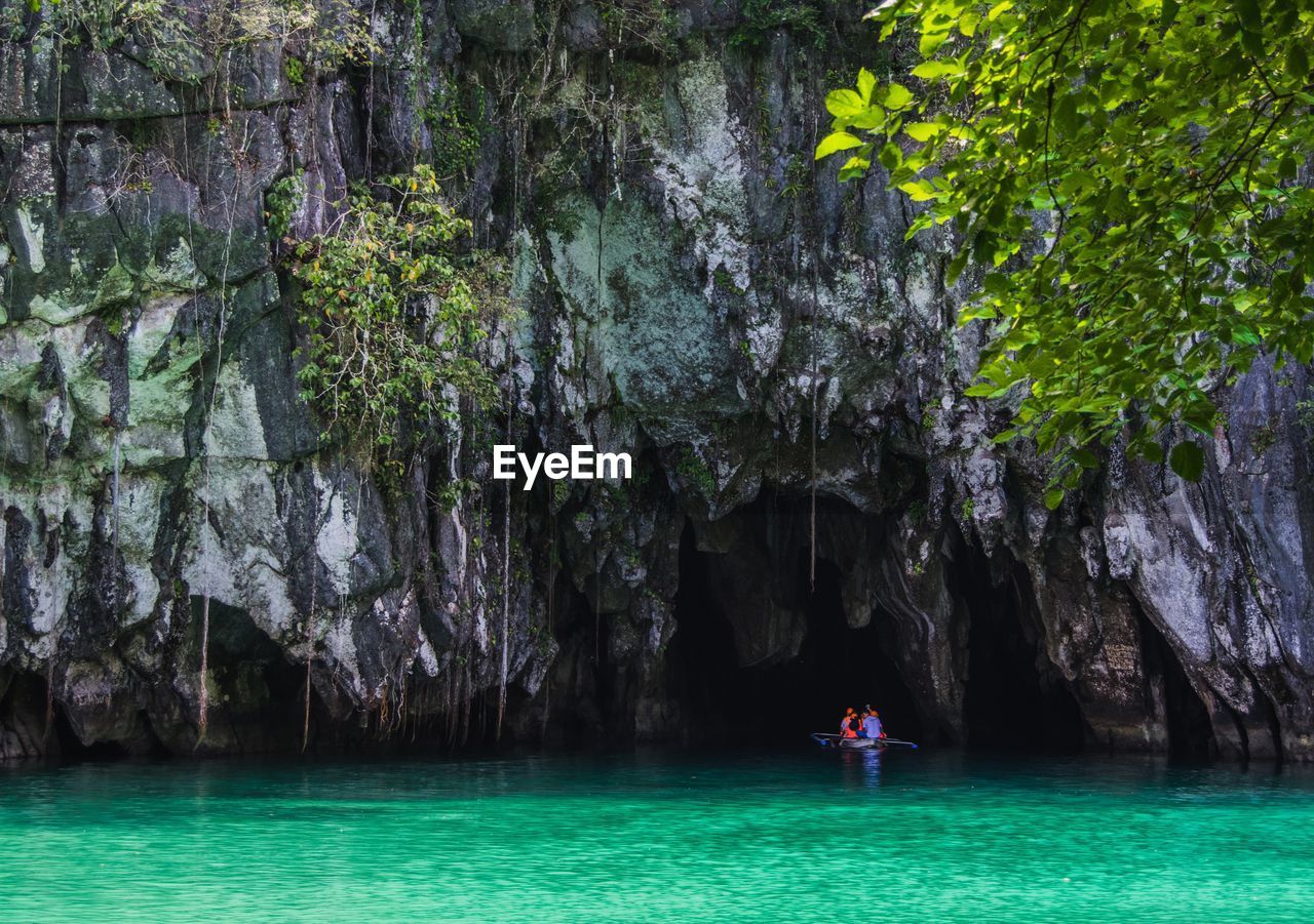 People on boat in sea against rock formation