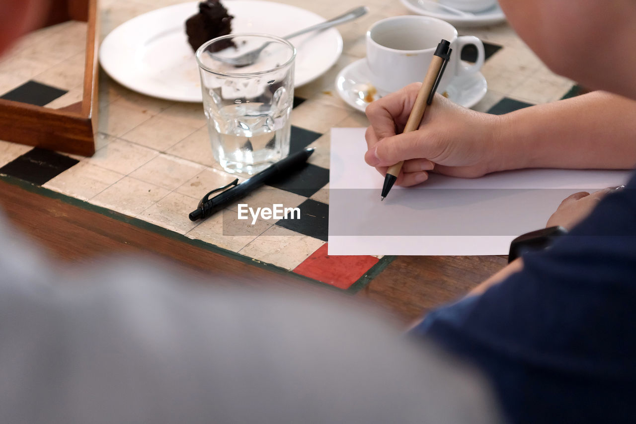 Midsection of woman writing on paper at table