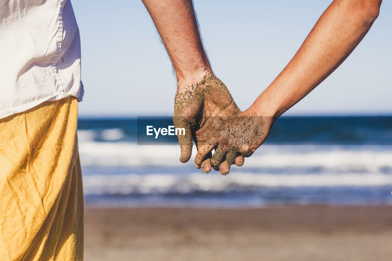 Midsection of couple holding hands on beach