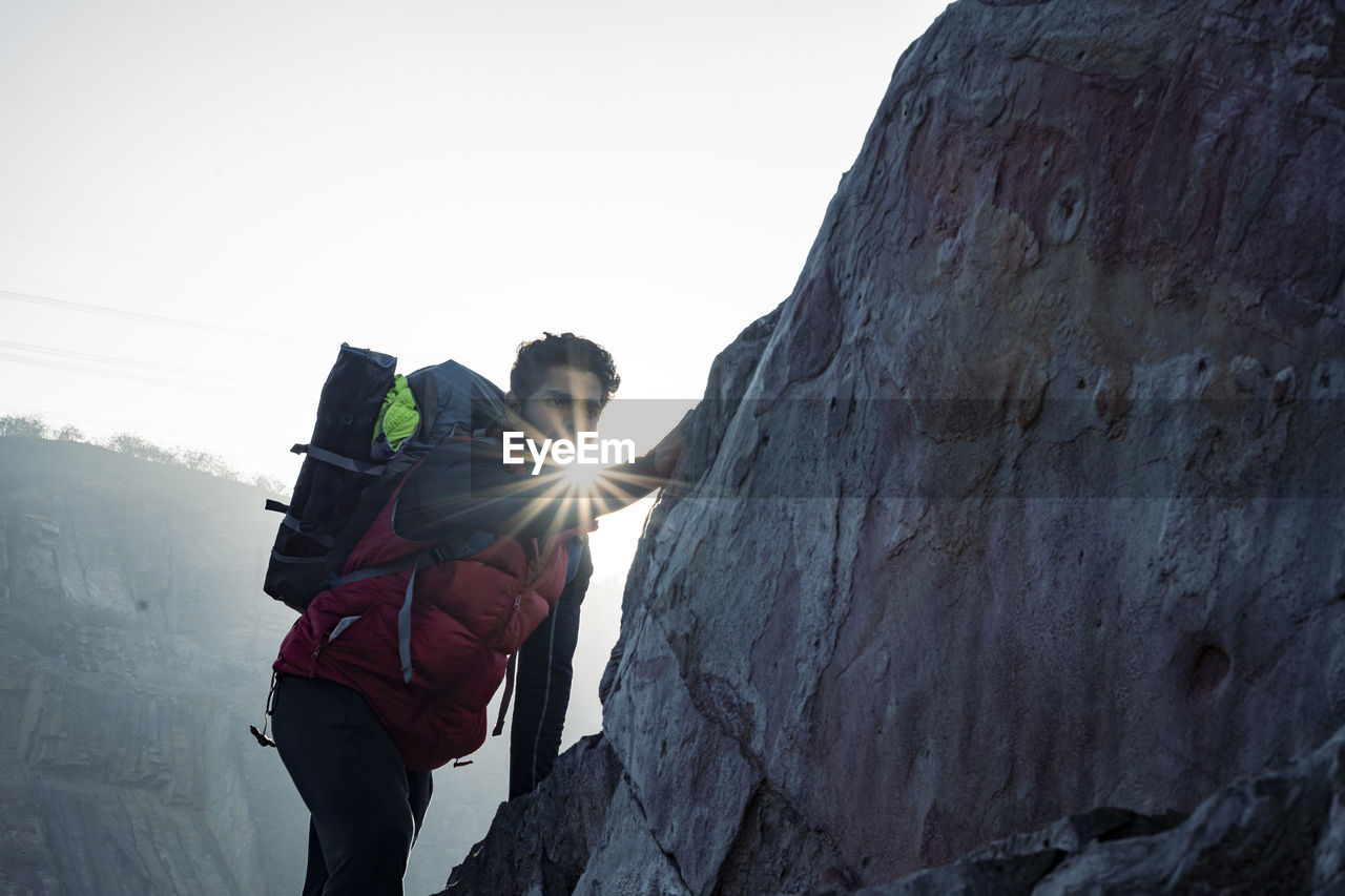 Young indian climber and traveler climbing up the mountain rock during sunset. adventure and sports.