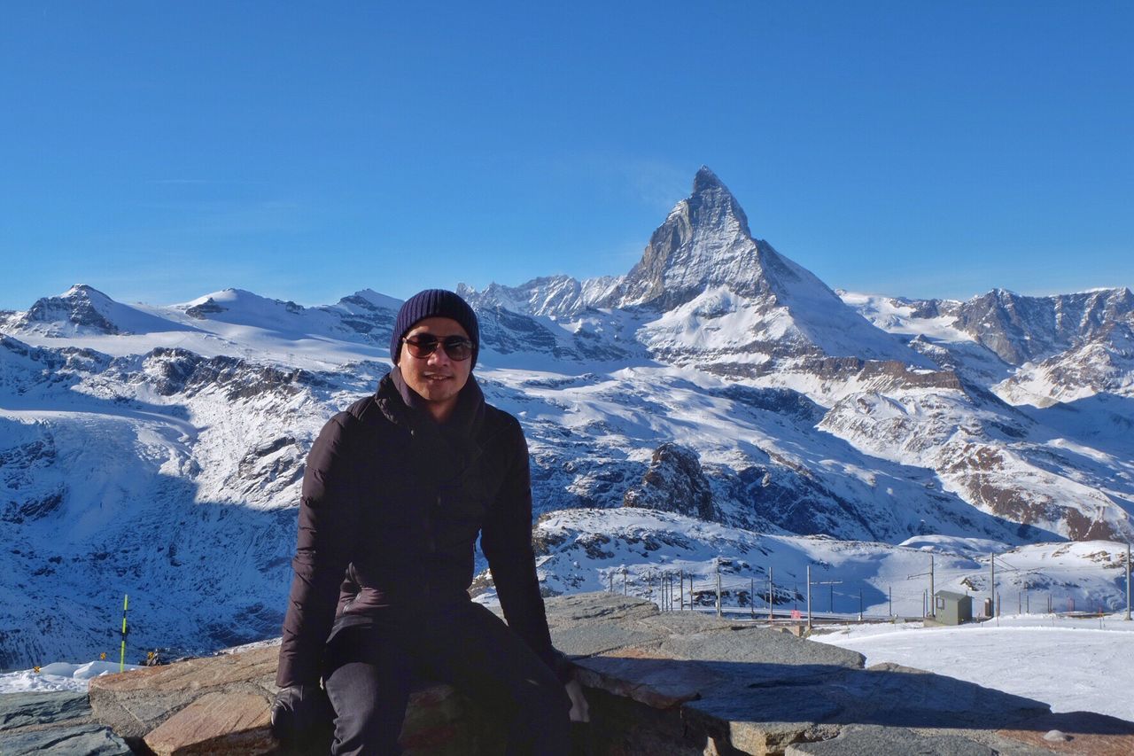 PORTRAIT OF MAN STANDING ON SNOWCAPPED MOUNTAINS AGAINST SKY