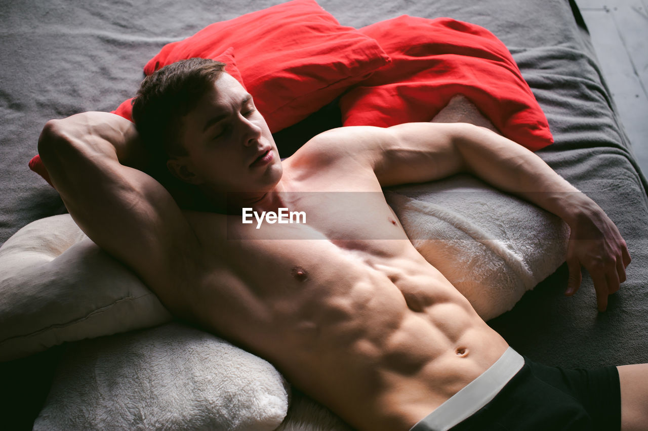 High angle view of shirtless man lying on bed at home