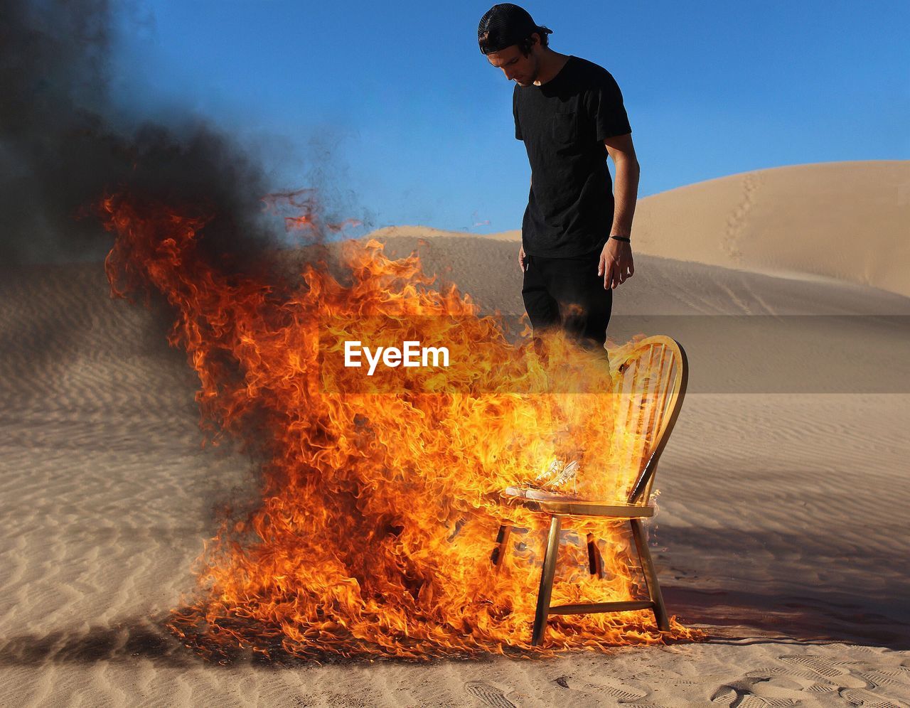 Young man standing on burning chair at desert