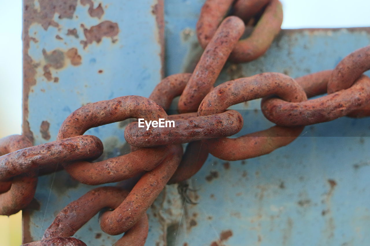 CLOSE-UP OF RUSTY METAL CHAIN ON WEATHERED WALL