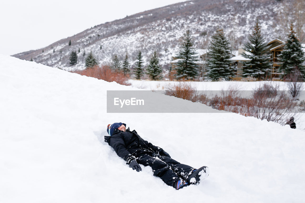 Full length of boy lying down on snow covered land during winter