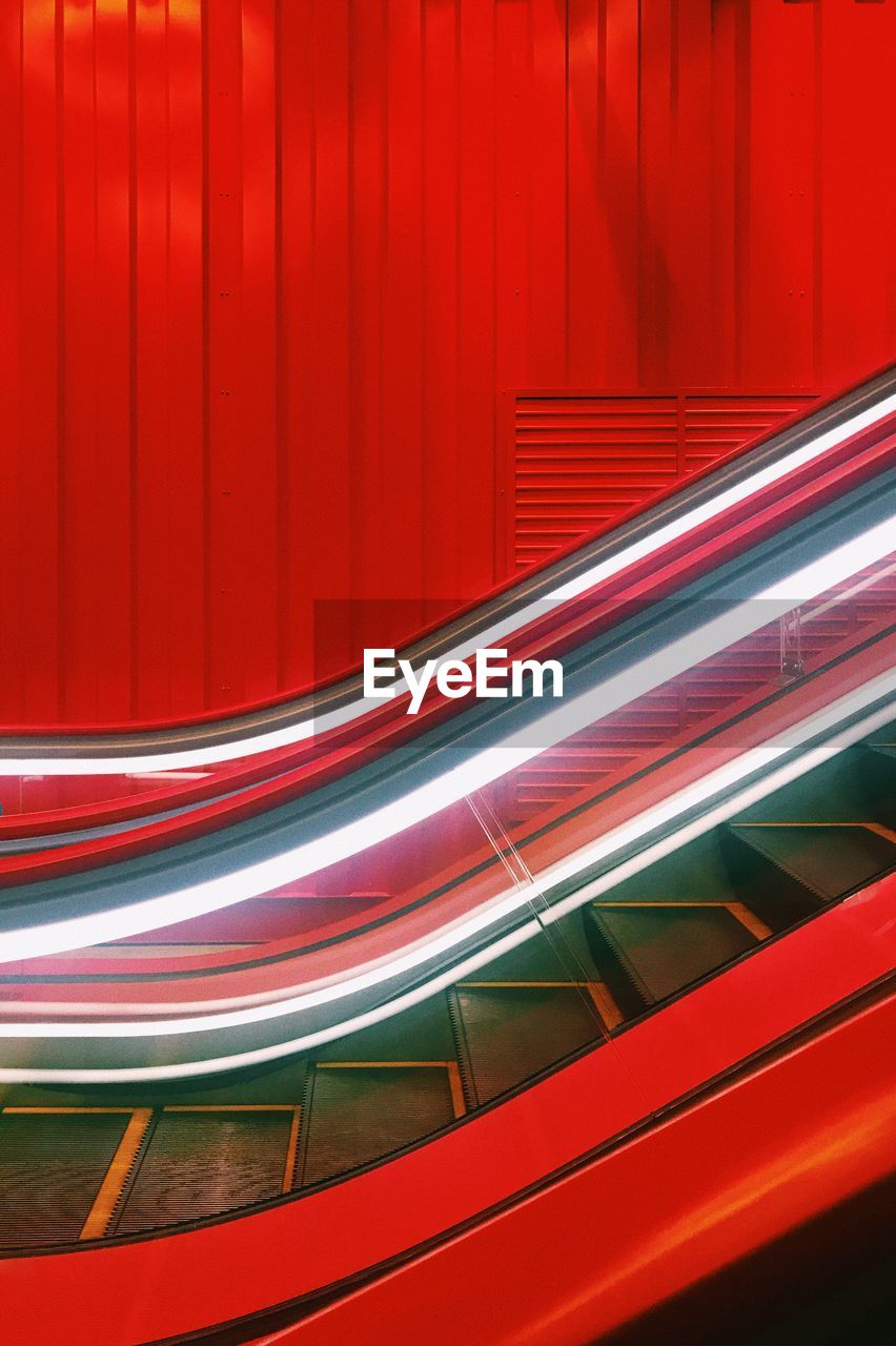 Close-up of illuminated escalator by red wall