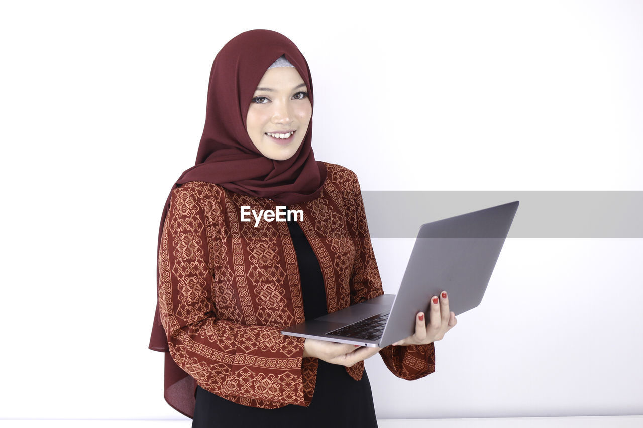 PORTRAIT OF YOUNG WOMAN USING PHONE AGAINST WHITE BACKGROUND