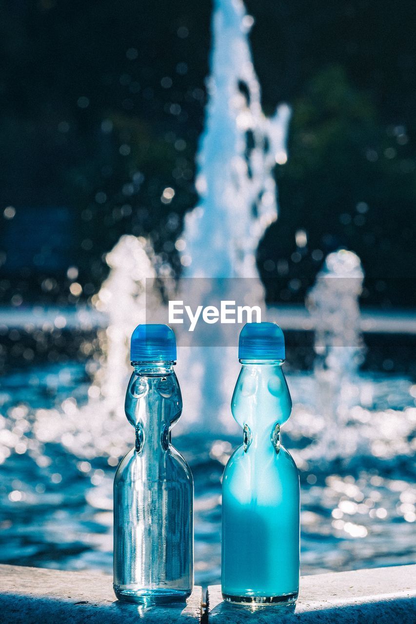 Close-up of water bottle against dancing fountain