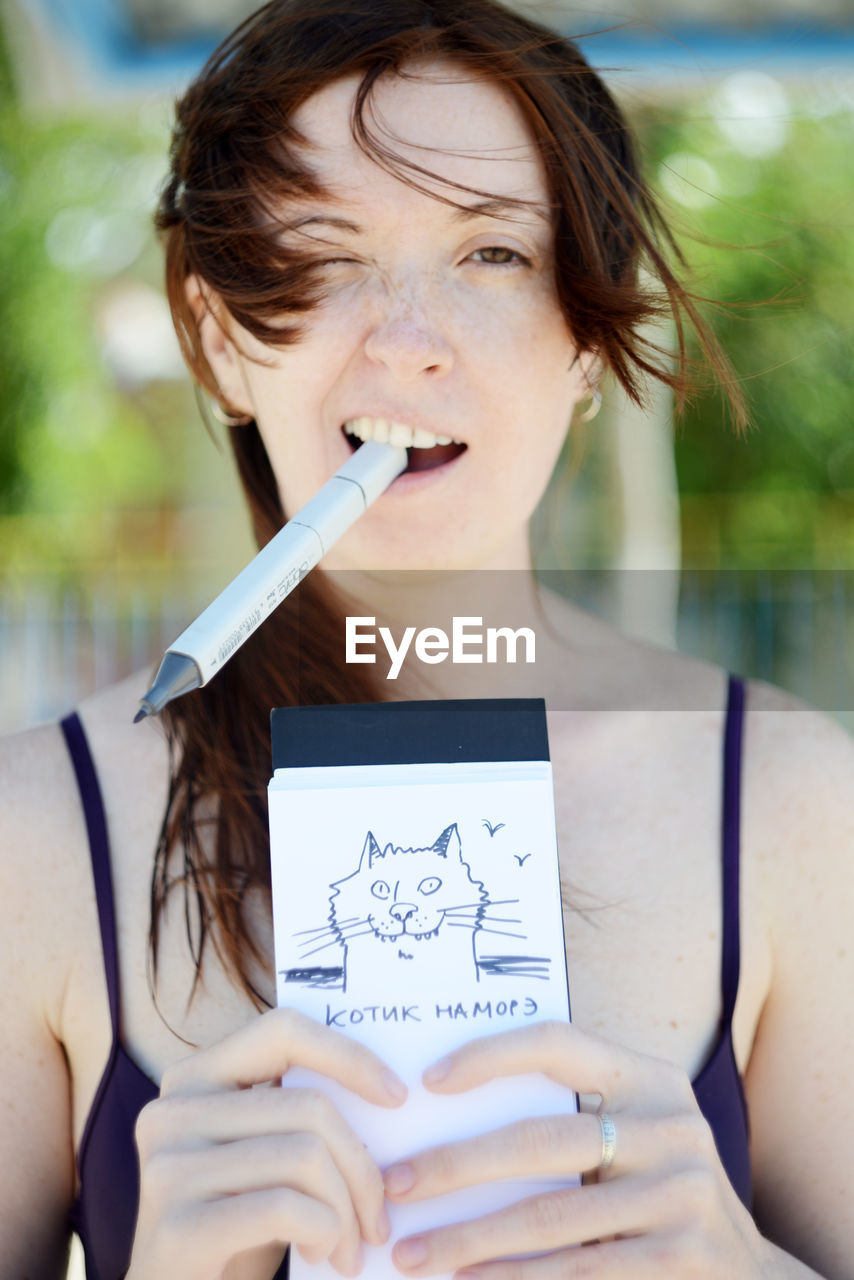 Portrait of cheerful woman holding cat drawing on notepad