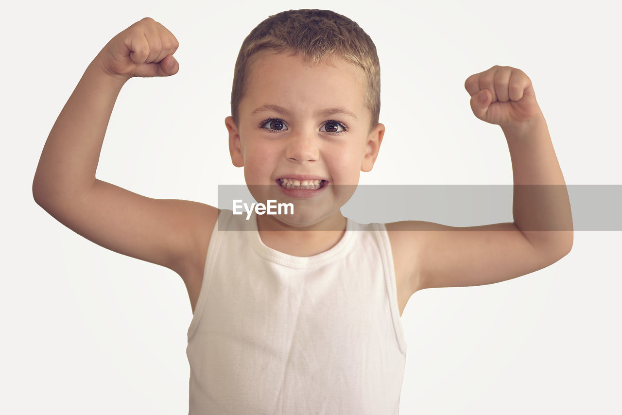 Portrait of boy flexing muscles against white background