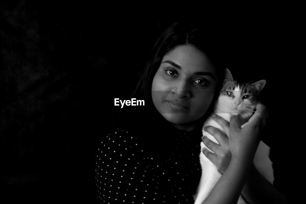 Portrait of woman holding cat against black background