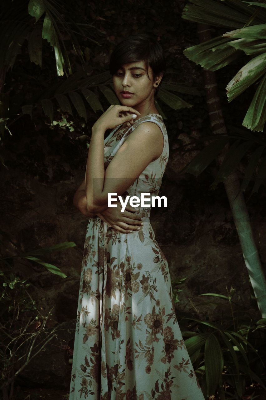 Young woman standing by tree in forest