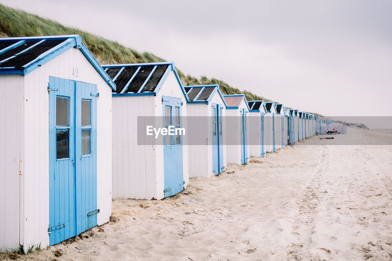 Huts in row at sandy beach against sky