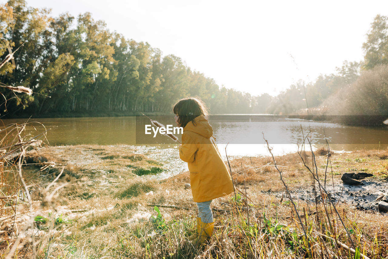 Full length of girl holding cattail standing by river