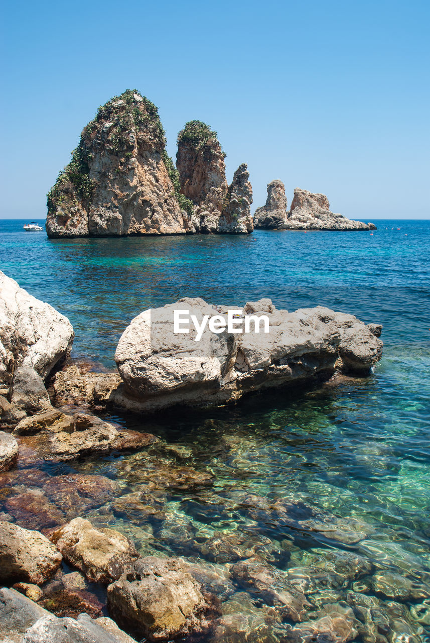 Scenic view of rocks in sea against clear blue sky