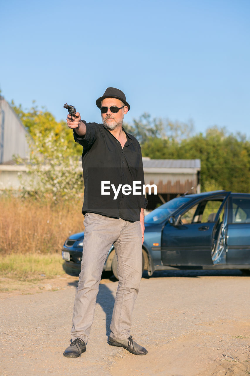 YOUNG MAN WEARING SUNGLASSES STANDING ON CAR