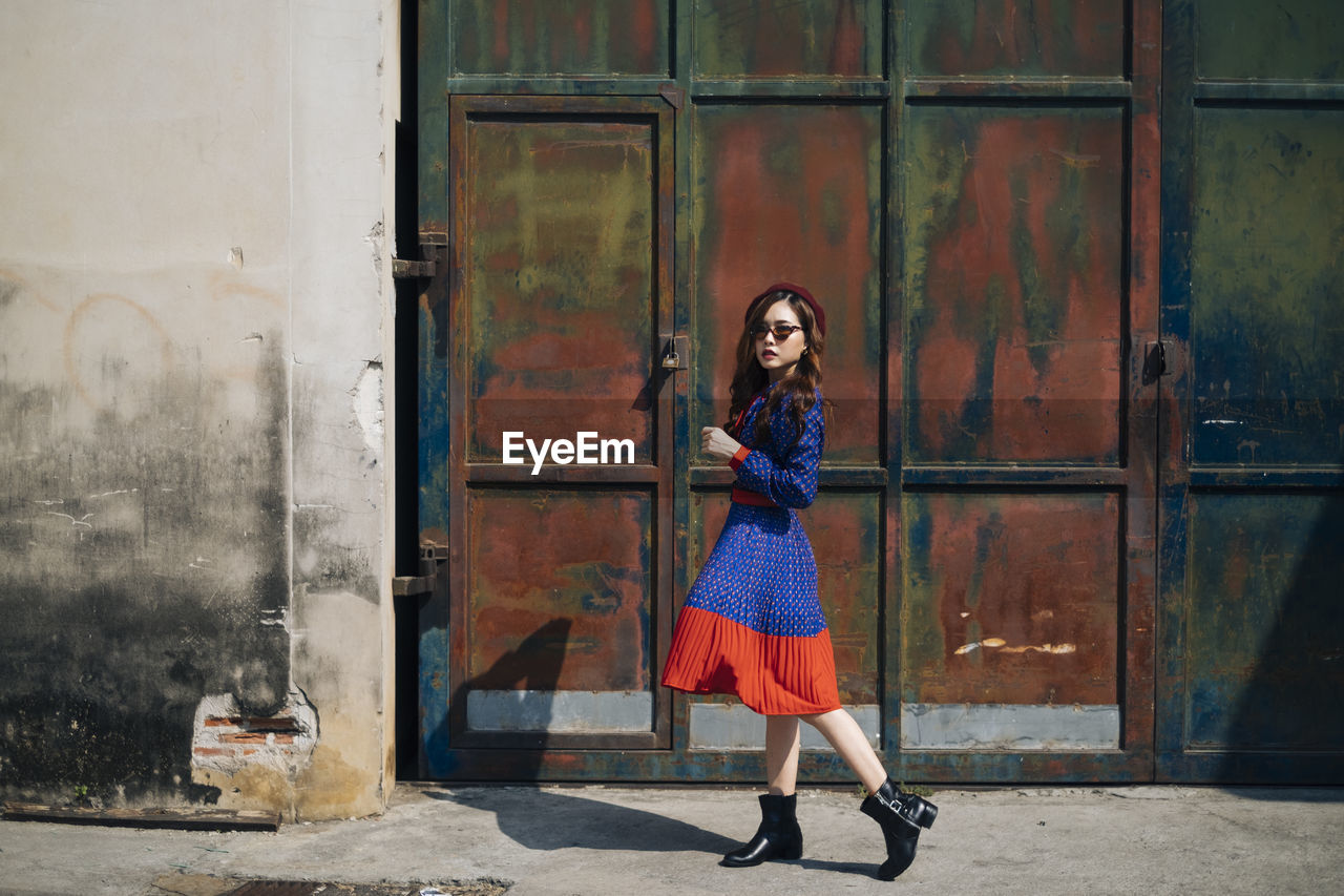 Full length portrait of young woman walking against metallic gate