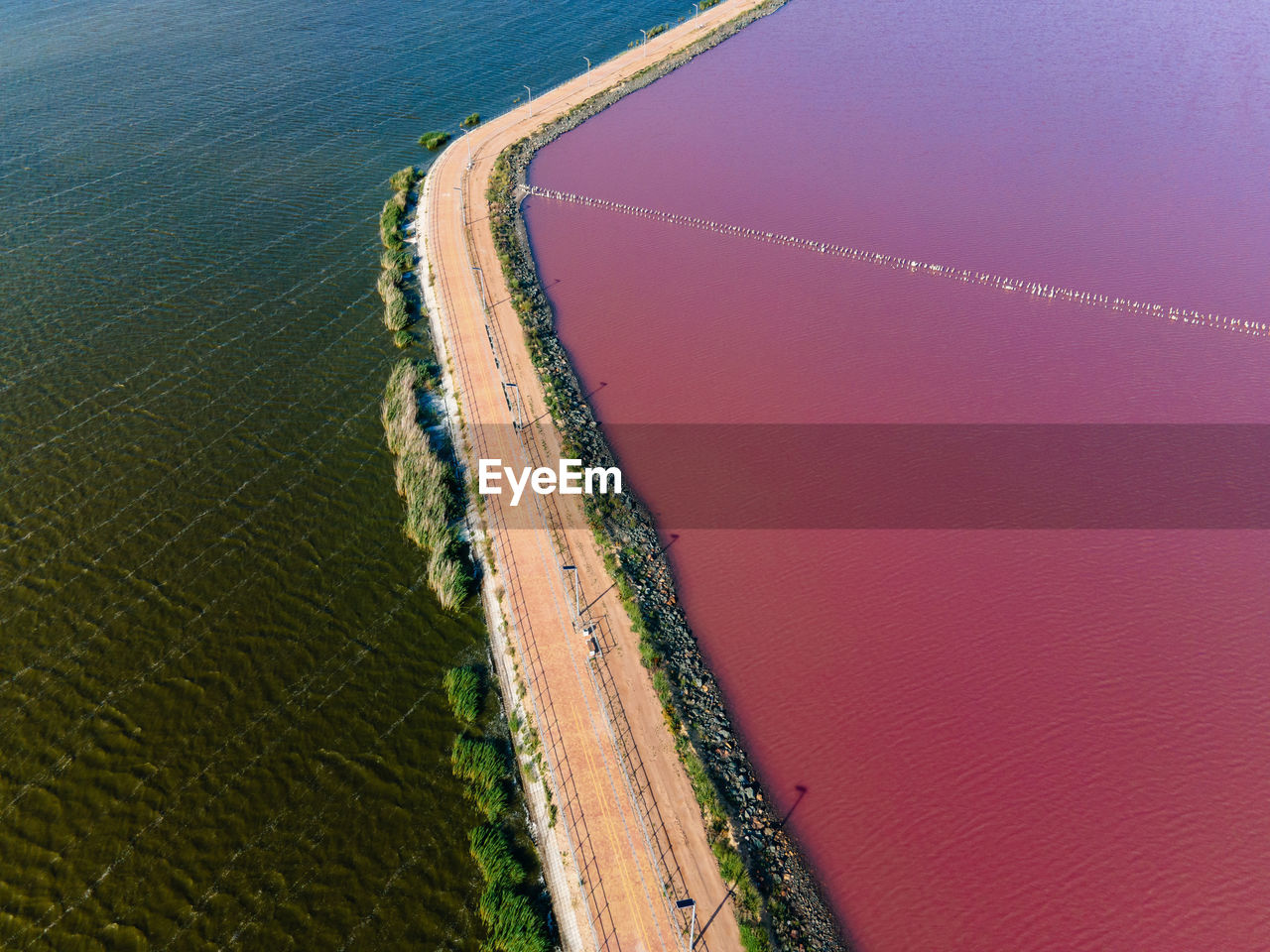 Road that separates the pink salt lake and the black sea view from the drone