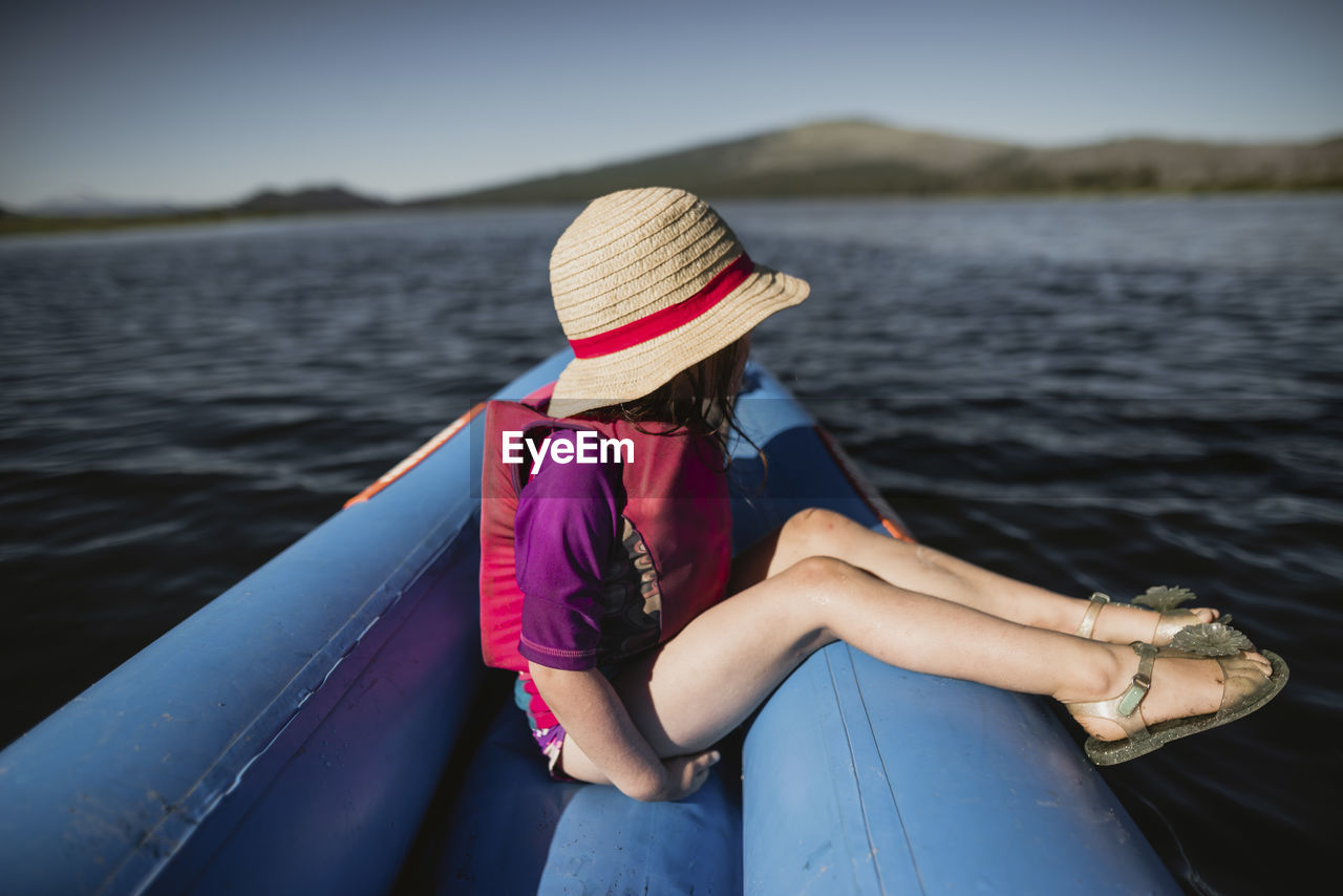 Side view of thoughtful girl wearing hat while sitting in inflatable raft on lake