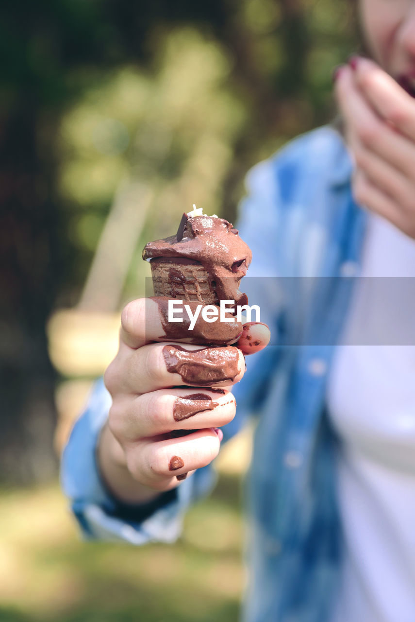 Midsection of young woman holding ice cream cone while standing outdoor