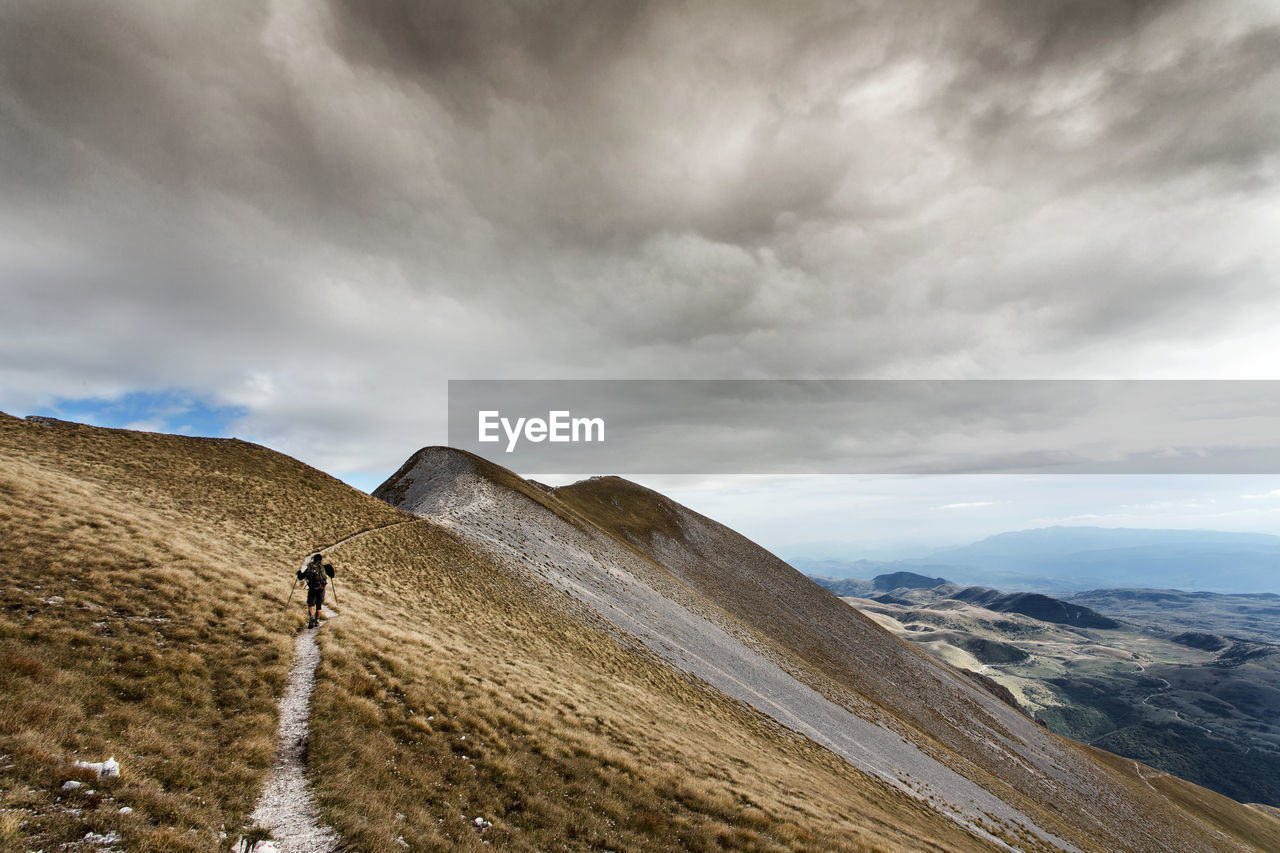 Hiker walking on mountain against cloudy sky