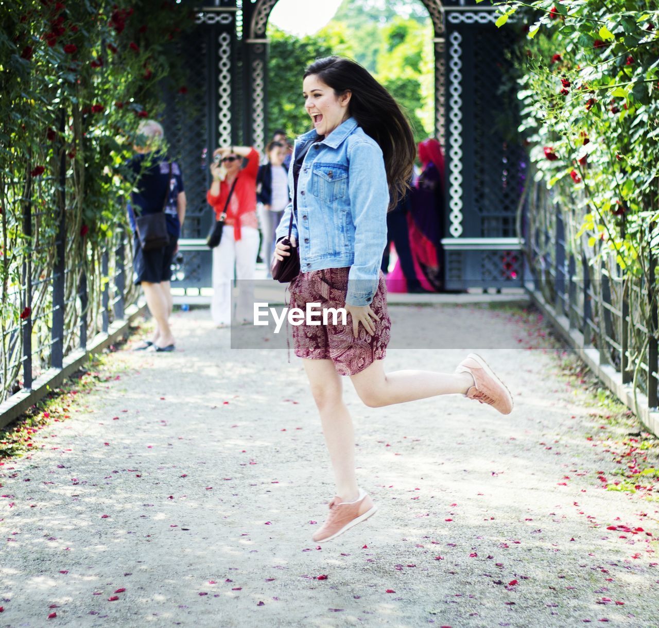 Cheerful woman jumping in mid-air on pathway amidst plants at park