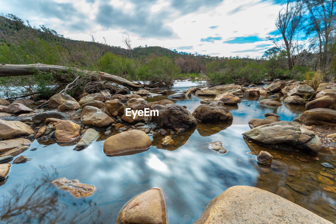 ROCKS IN RIVER BY STREAM AGAINST SKY