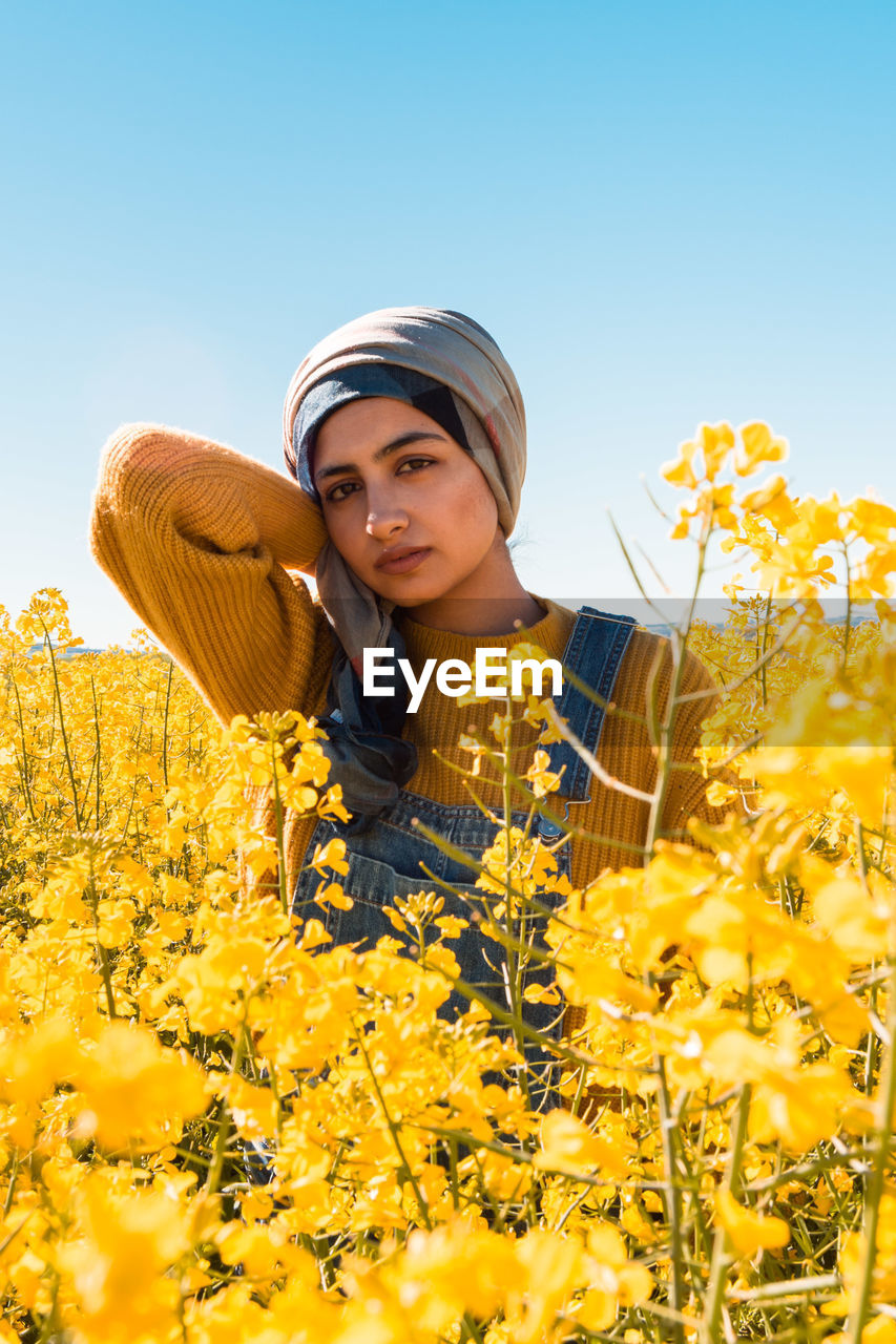 Portrait of young woman by yellow flowering plants against clear sky