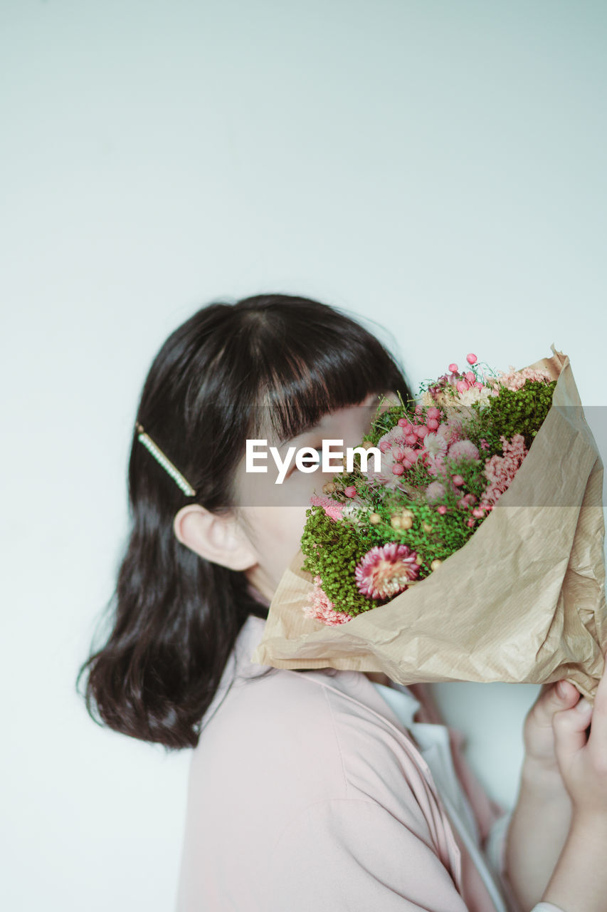 Portrait of woman holding bouquet against white background