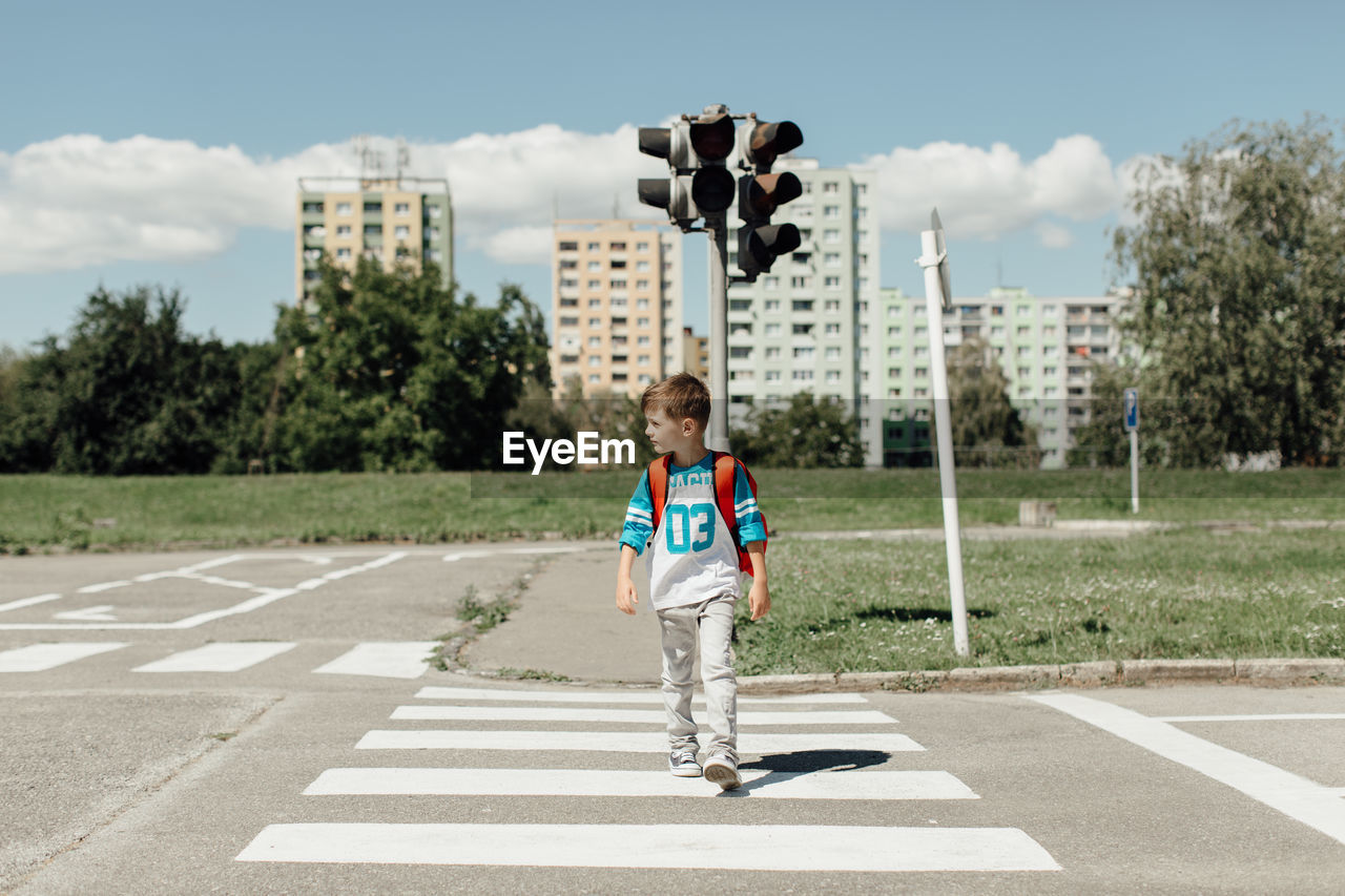 BOY WALKING ON ROAD AGAINST SKY