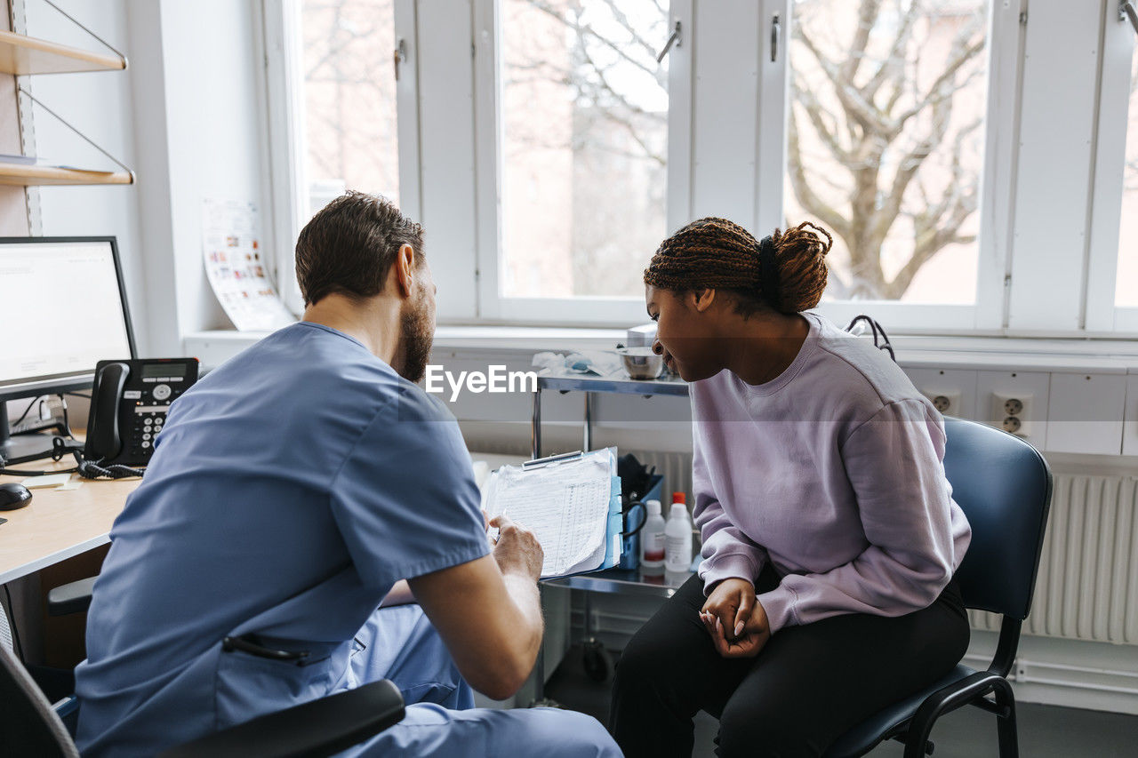 Male doctor discussing reports with female patient during visit at hospital