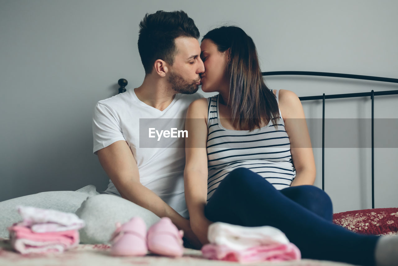 Man kissing pregnant women while sitting on bed at home