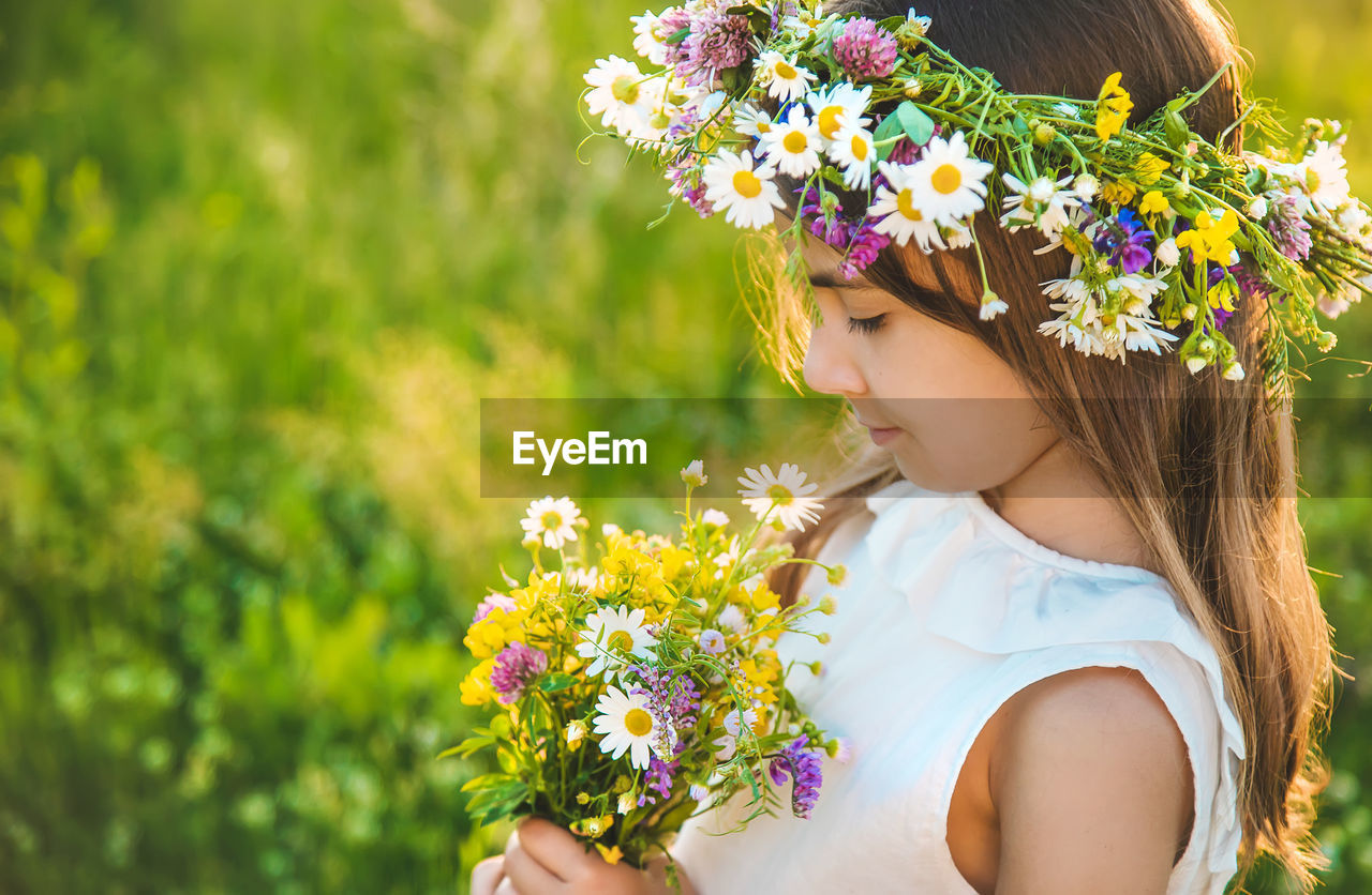 Side view of girl wearing floral crown holding flowers