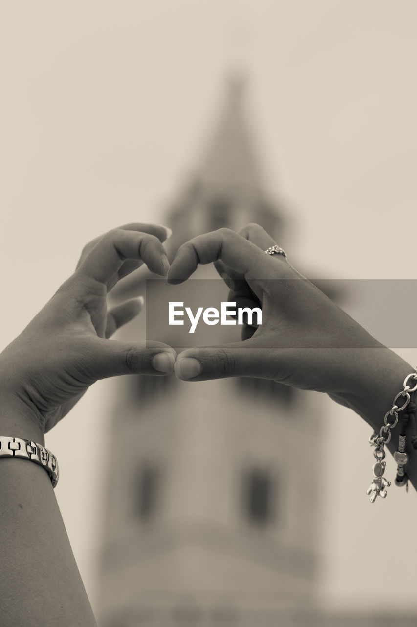 Close-up of hands forming heart shape against building