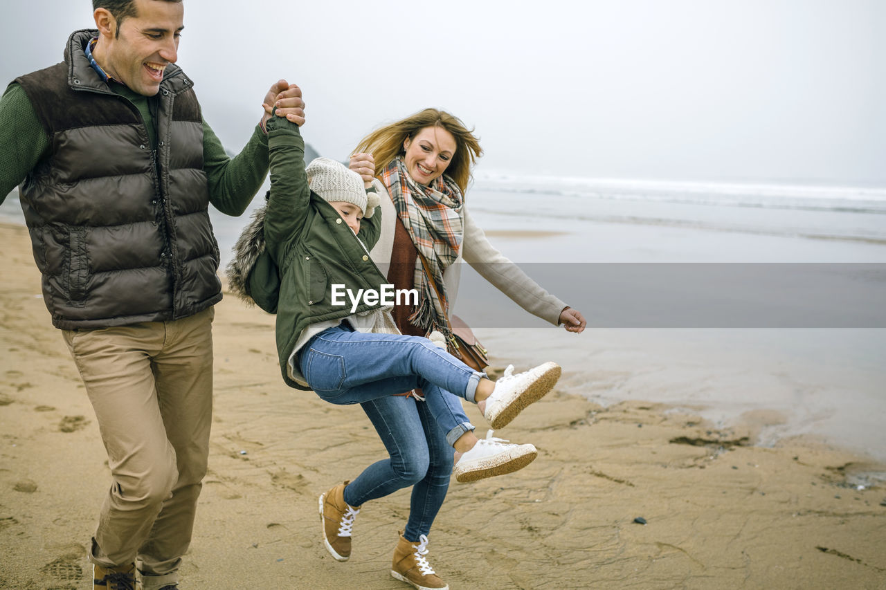 Happy parents lifting up daughter on the beach in winter