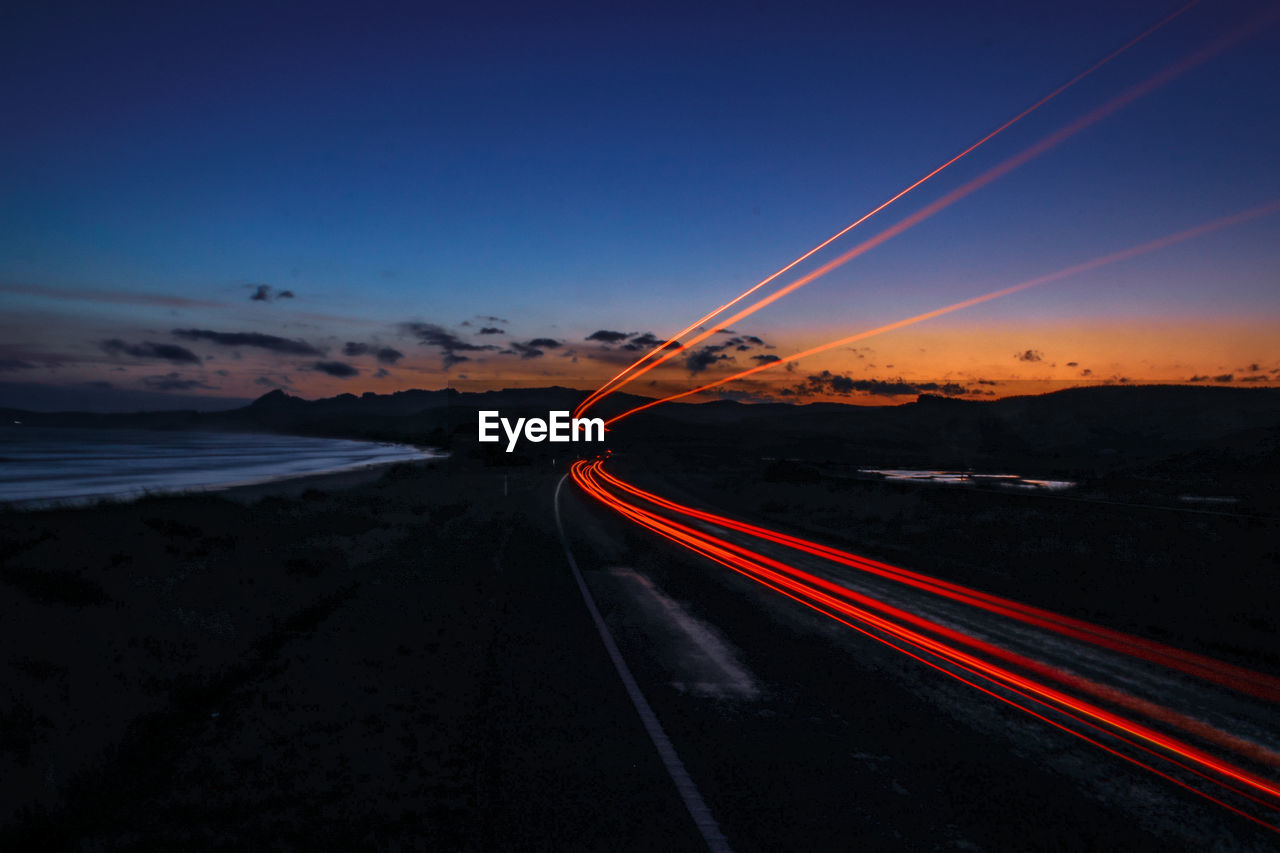 Light trails on road against sky during sunset