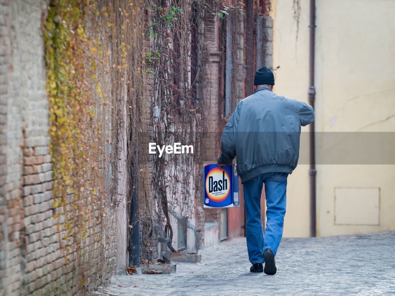 REAR VIEW OF A MAN WITH UMBRELLA WALKING ON STREET