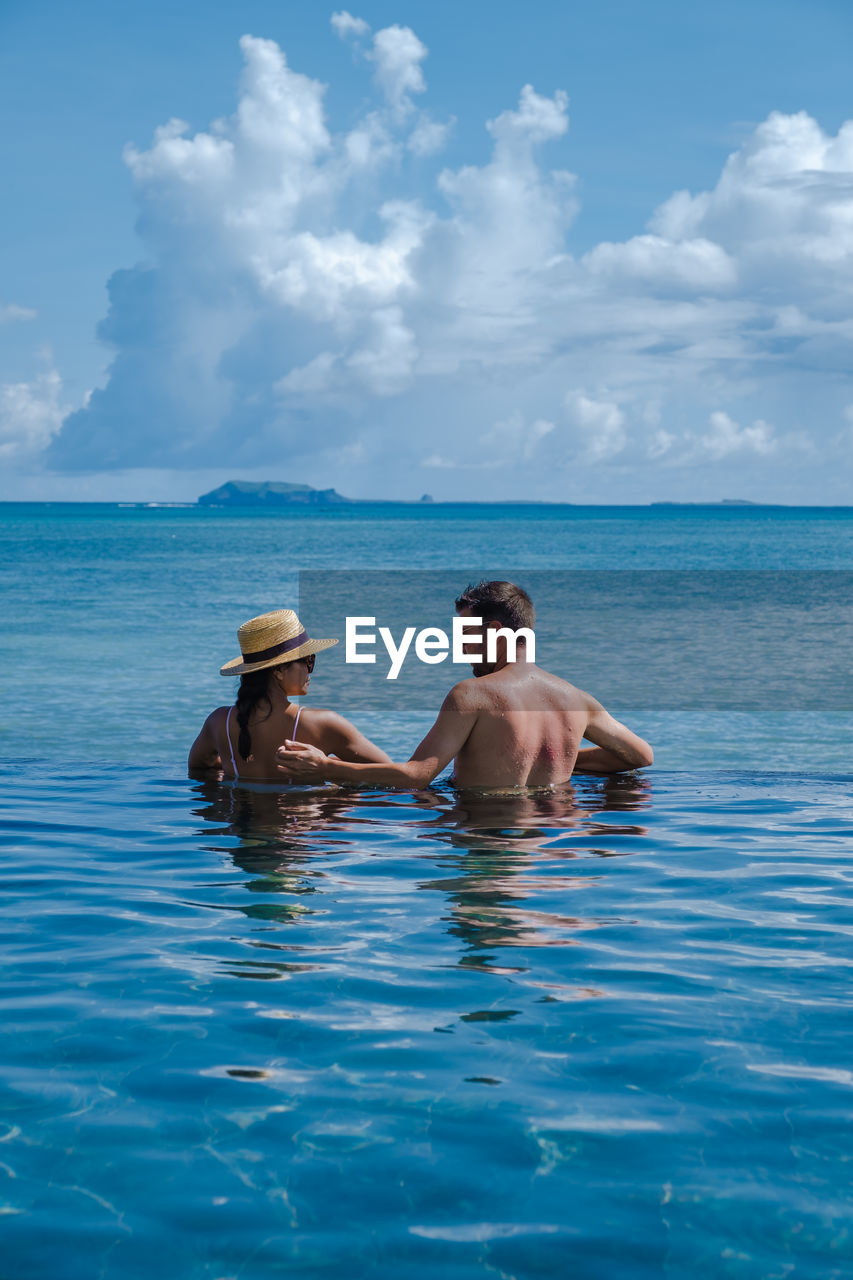 Rear view of woman and man swimming in infinity pool against sea