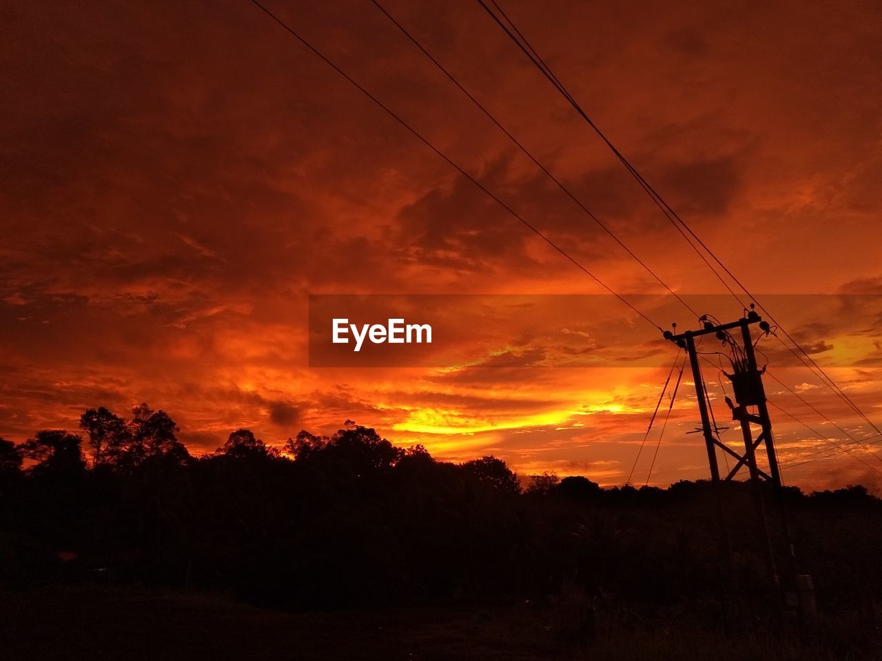 SILHOUETTE ELECTRICITY PYLONS ON LANDSCAPE AGAINST ORANGE SKY