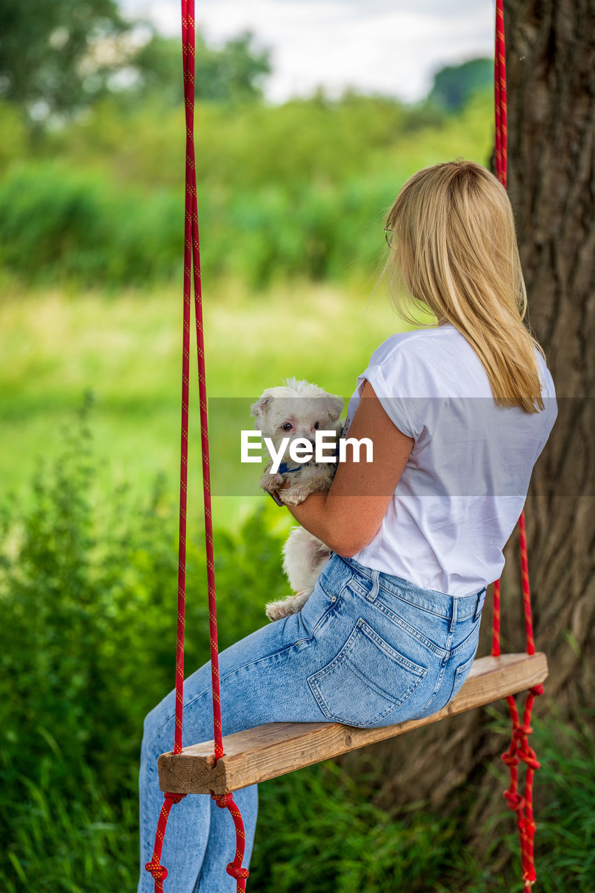 Young woman with a white dog on a tree swing.