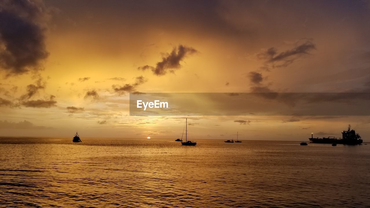 Silhouette boats sailing in sea against sky during sunset