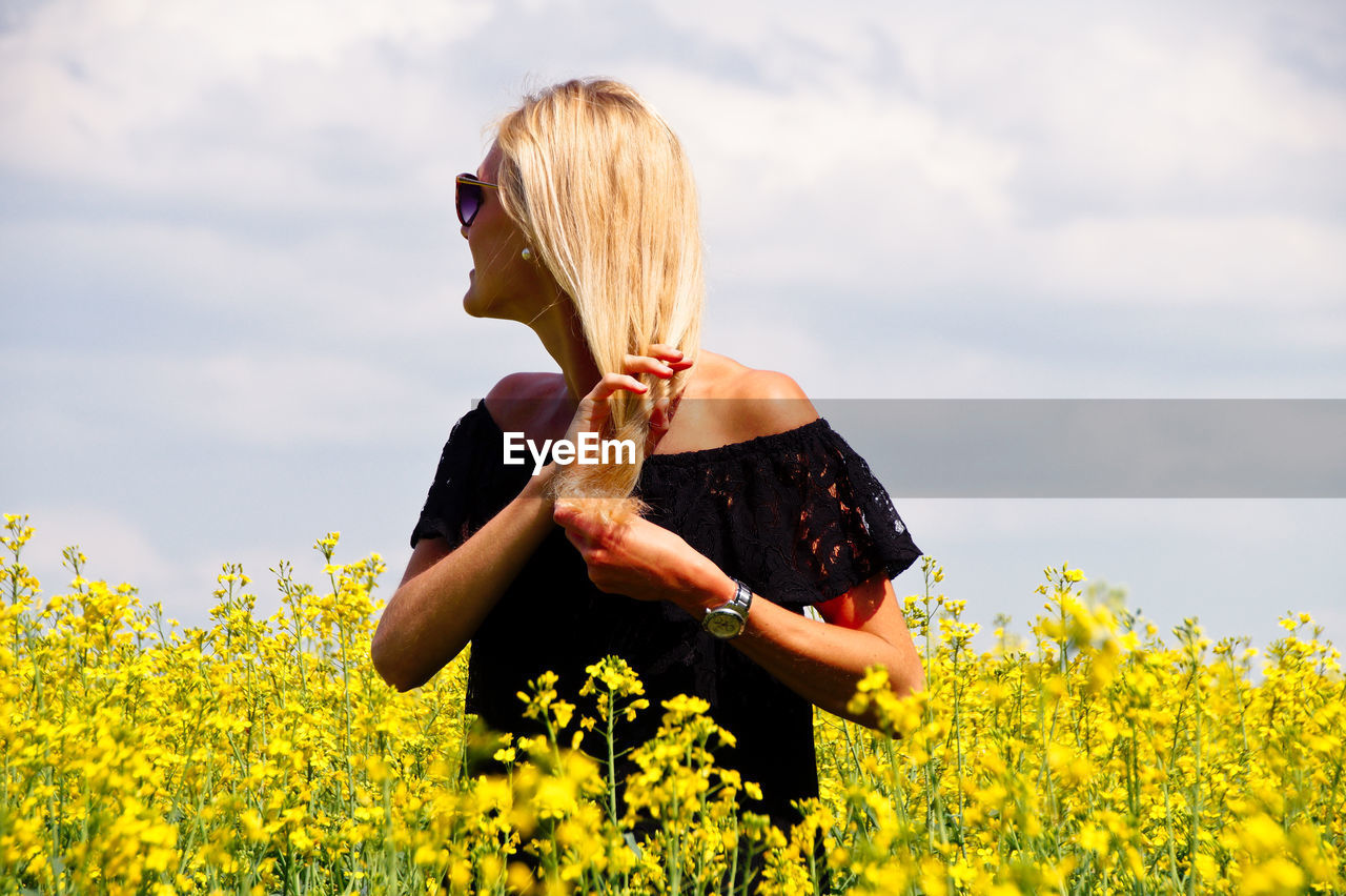Smiling young woman with hand in hair standing on oilseed rape field