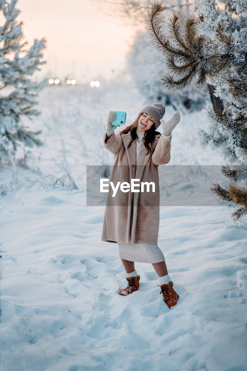 A girl in a beige faux fur coat tooks selfie in a snowy forest. beautiful fairy winter in the forest