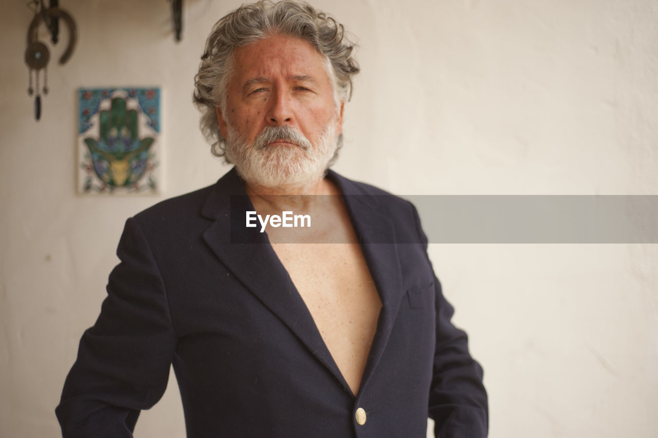 Portrait of senior man wearing blazer standing against wall at home