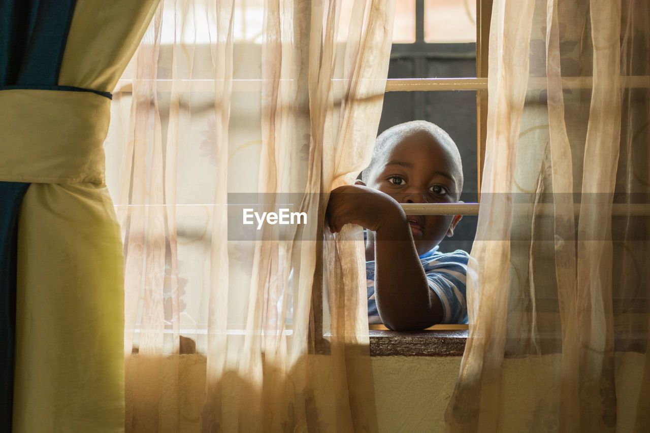 Portrait of boy peeking through window at home