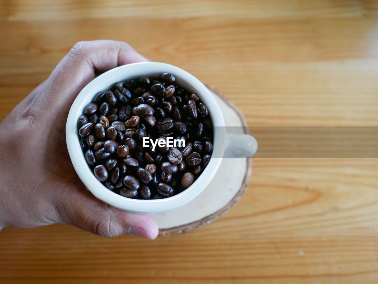 HIGH ANGLE VIEW OF HAND HOLDING COFFEE CUP ON TABLE