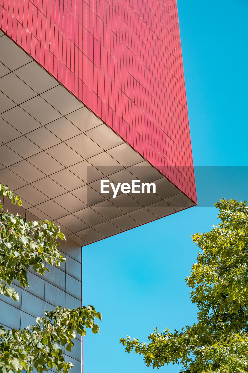 Red angular building against blue sky and trees 