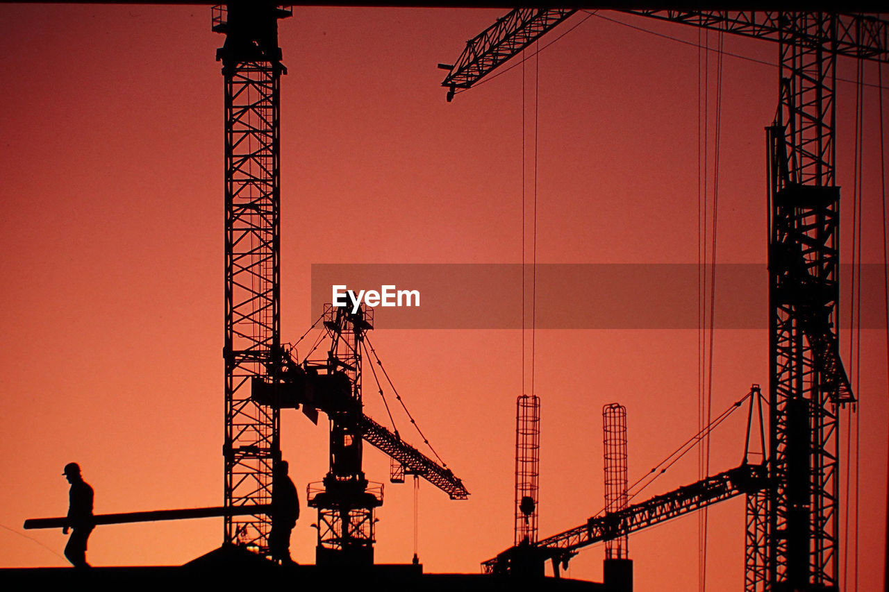 Silhouette of cranes against sky at sunset