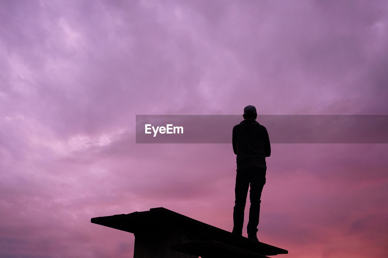 low angle view of silhouette man standing against cloudy sky during sunset