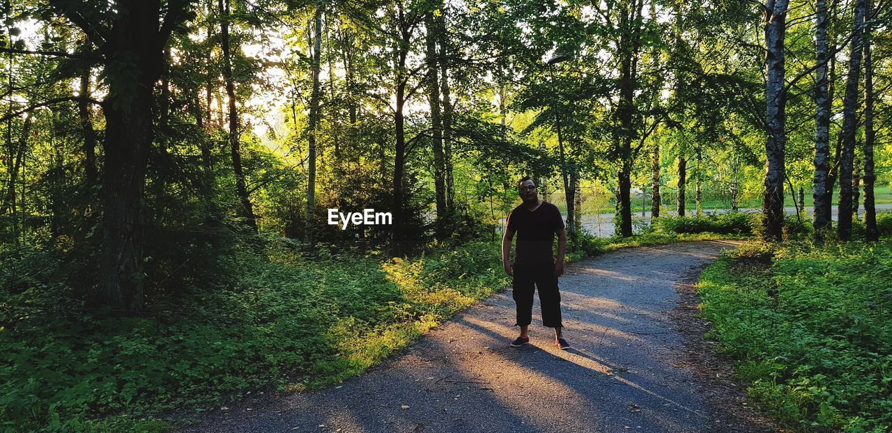 Portrait of mid adult man standing on road amidst trees in forest